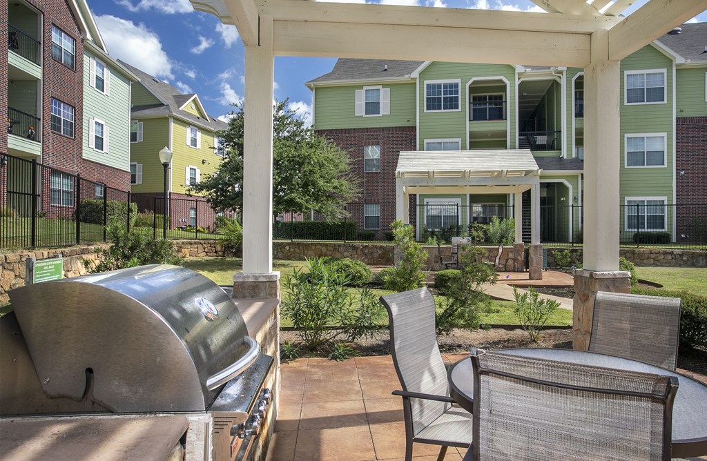 Dog-Friendly Apartments in Tyler, TX - Covered Community BBQ Area with Counter Space, Table and Seating, and Lush Landscaping.