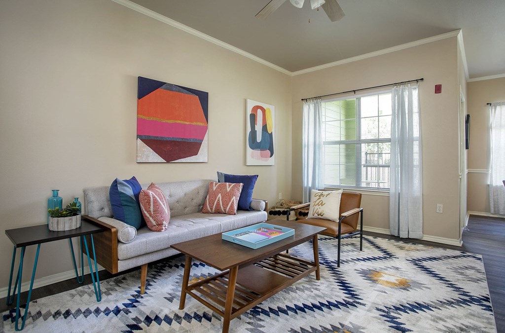 Apartments for Rent Tyler, TX - Spacious Living Room with Plank Wood Flooring, a Large Window, a Ceiling Fan, and Neutral Painted Walls.