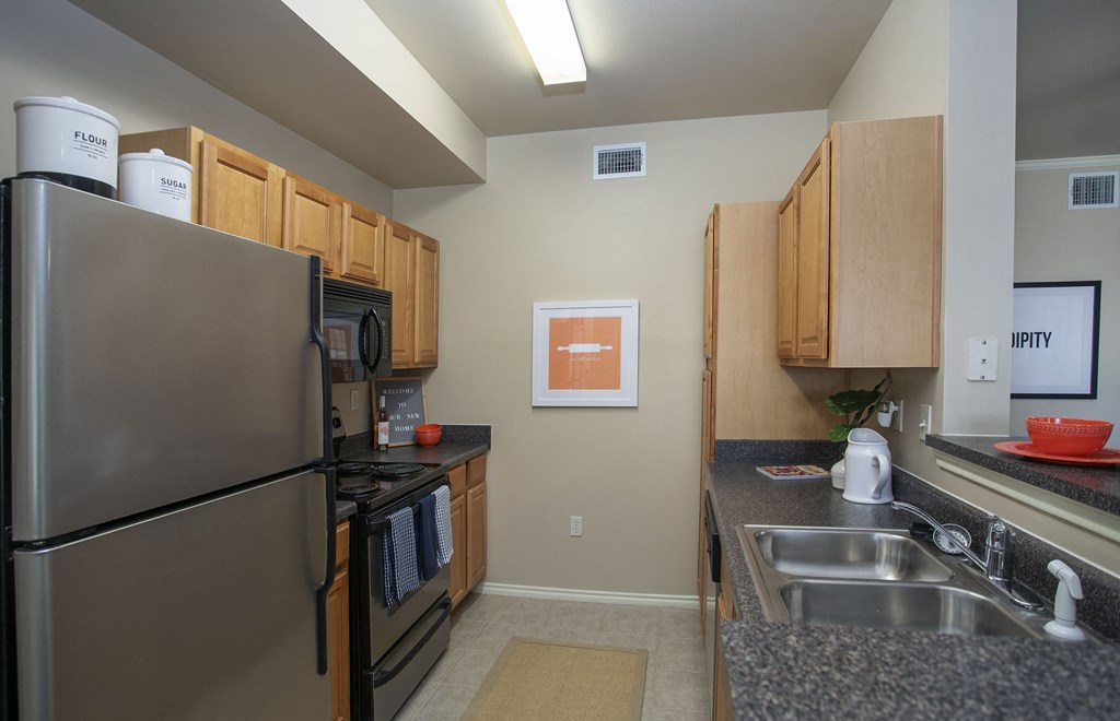 Pet-Friendly Apartments In Tyler, TX - Kitchen with Stainless Steel Appliances, Breakfast Bar, Ceramic Tile Flooring, Microwave, Fridge, And Oven.