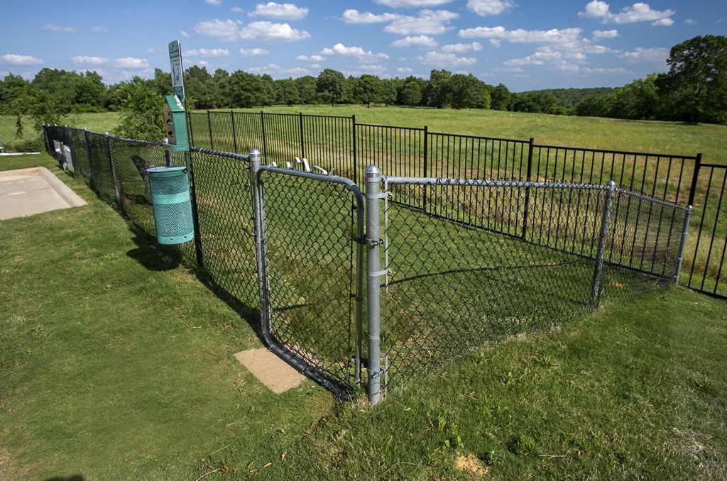 Apartments For Rent Tyler, TX - Gated Dog Park With Lush Grass, Bench, And Trashcan.