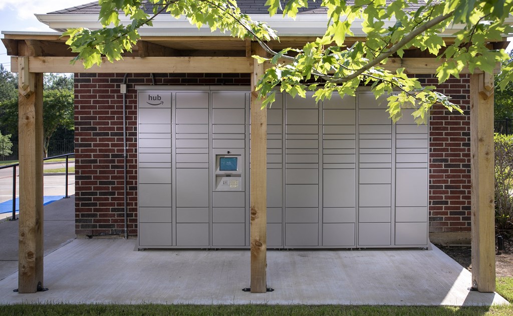 Apartments for Rent in Tyler, TX - Outdoor Covered Amazon Package Hub Surrounded by Greenery and Near a Parking Lot.