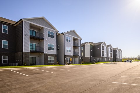 A row of modern apartment buildings with a parking lot in front.