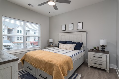 A bedroom with a bed, nightstand, and window overlooking a street.