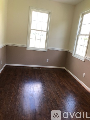 A room with brown wooden floors and two windows.