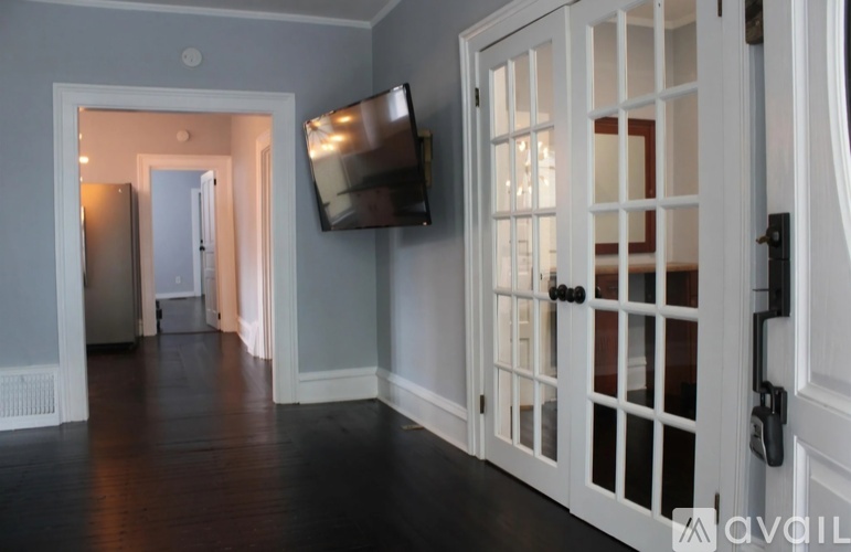 A hallway with a television mounted on the wall and a door with a glass panel.