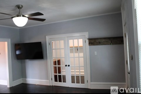 A room with a ceiling fan and a flat screen TV mounted on the wall.