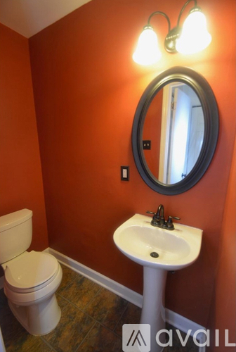 A bathroom with orange walls, a white toilet, and a white pedestal sink.