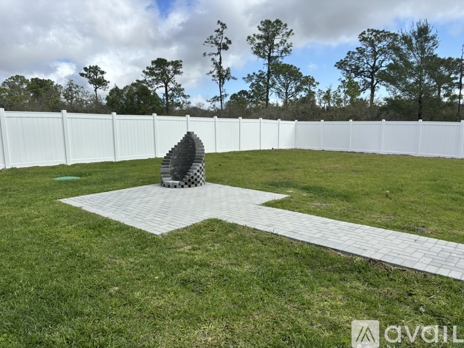 A white fence encloses a grassy area with a sculpture in the center.