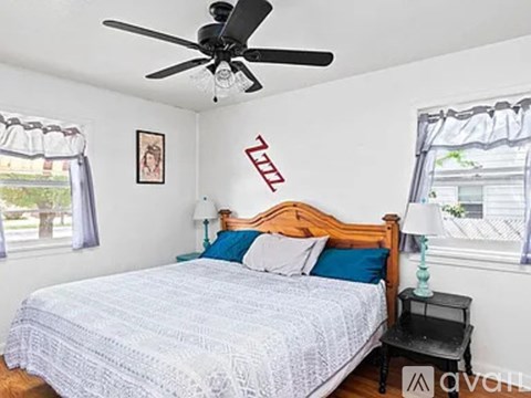 A bedroom with a bed, a ceiling fan, and a window with curtains.