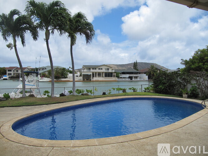 A pool surrounded by palm trees and a house in the background.