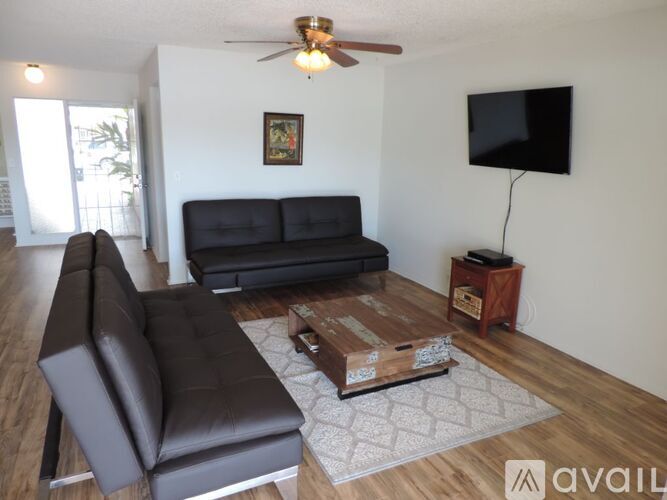 A living room with a black couch and a television on the wall.