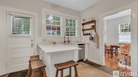 A kitchen with white cabinets and a white island with a wooden stool in front of it.