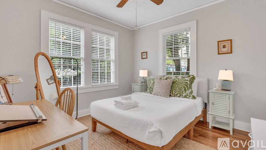 A bedroom with a bed, a chair, and a table with a lamp on it.