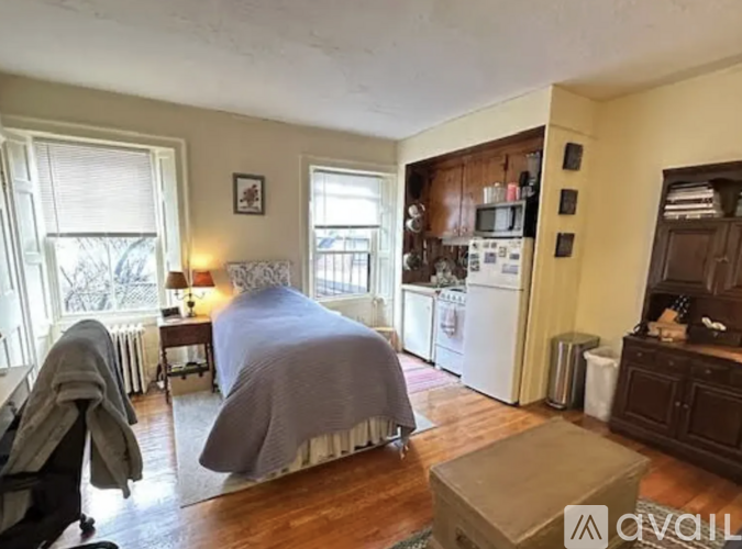 A bedroom with a bed covered in a grey blanket and a window with blinds.
