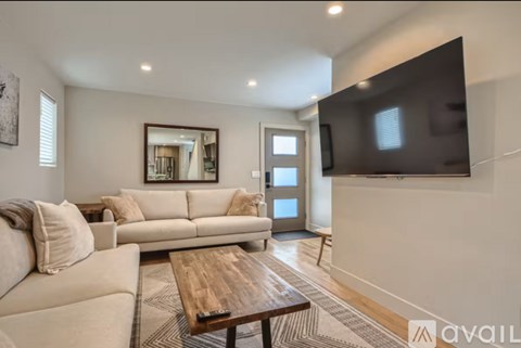 A living room with a couch, a coffee table, and a television mounted on the wall.