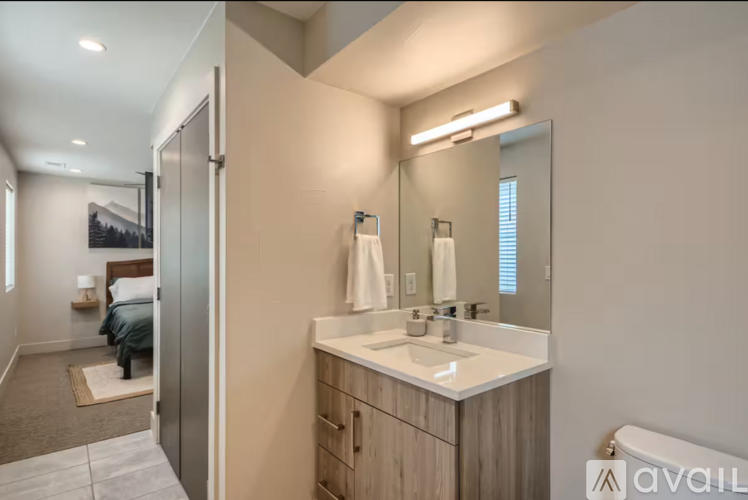 A bathroom with a sink, mirror, and a bedroom with a bed and a nightstand.