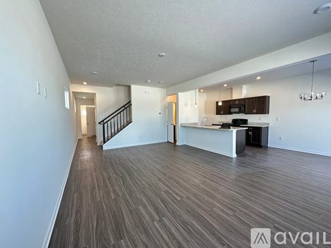 A spacious living room with wood flooring and a kitchen area in the background.
