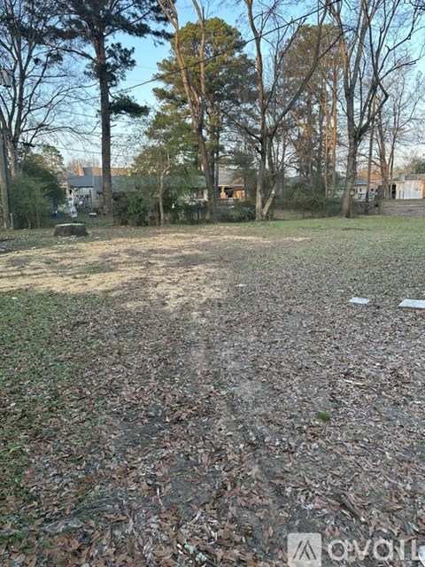 A field with trees and a house in the background.