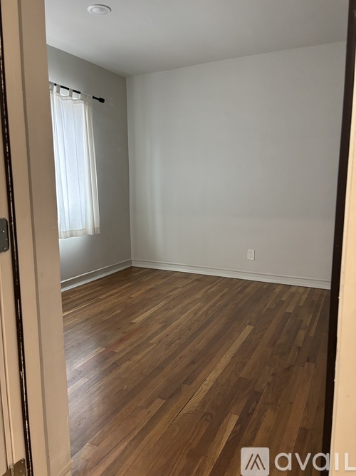 A room with wooden flooring and a window with white curtains.