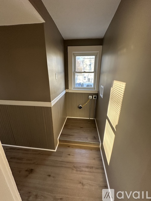 A hallway with wooden floors and a window with blinds.