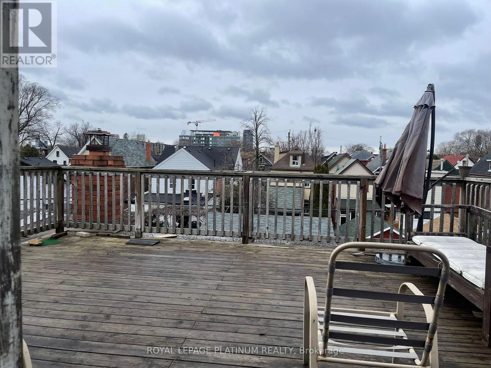 A wooden deck with a chair and umbrella in the foreground and buildings in the background.