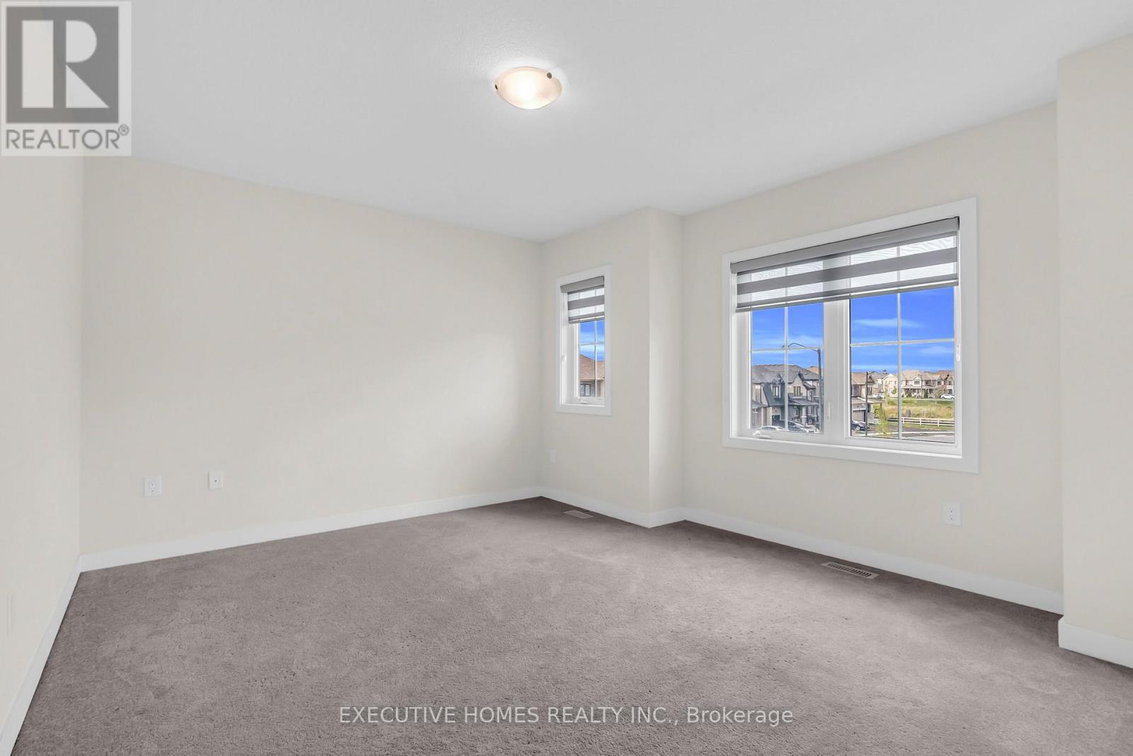 A room with a carpet floor and a window showing a view of buildings outside.