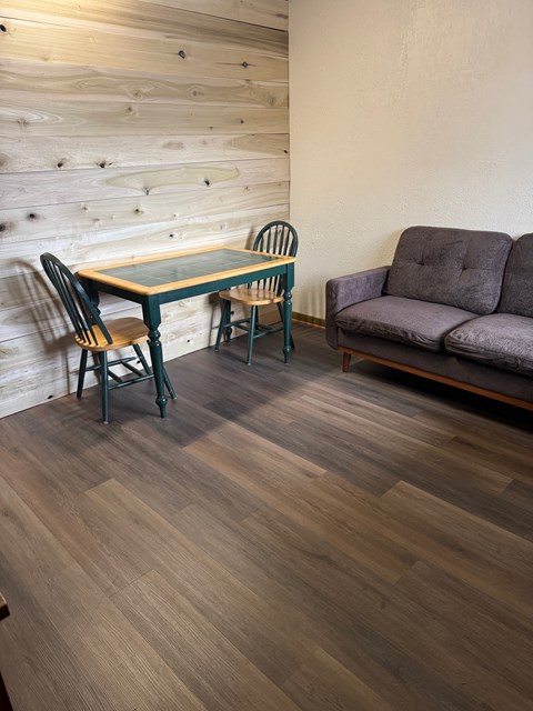 A grey couch sits next to a table with a chair.