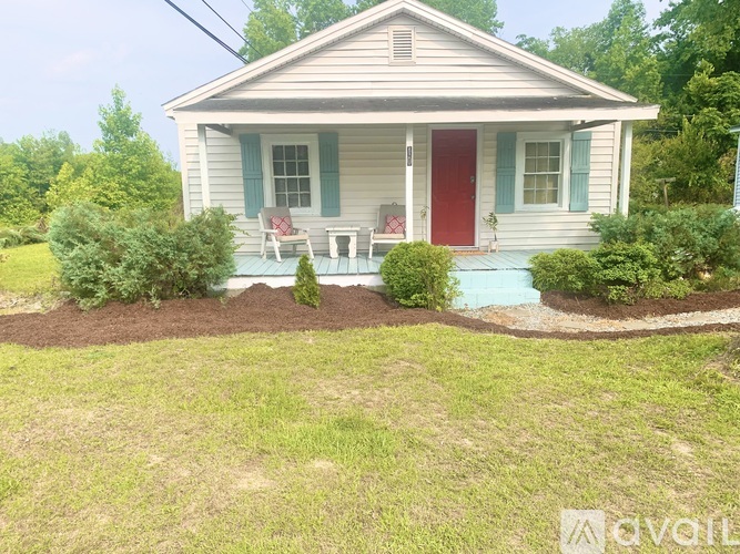 A small house with a red door and a red chair on the porch.