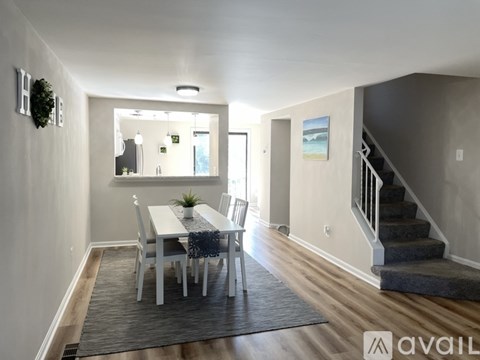 A dining room with a white table and chairs, a wreath on the wall, and a staircase in the background.