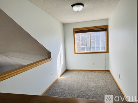 A room with a carpeted floor, a window with a view of a building, and a light fixture on the ceiling.