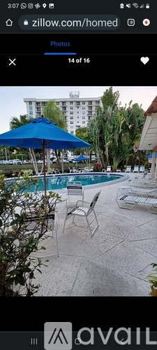 A blue umbrella is in the foreground of a pool area.