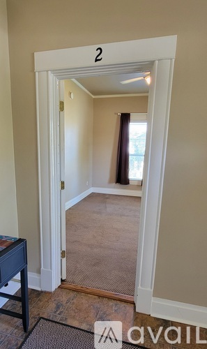 A room with a doorway leading to another room, with a table and a rug in the foreground.