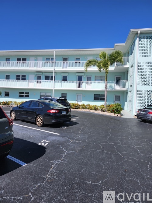 A black car is parked in a parking lot in front of a light blue building.