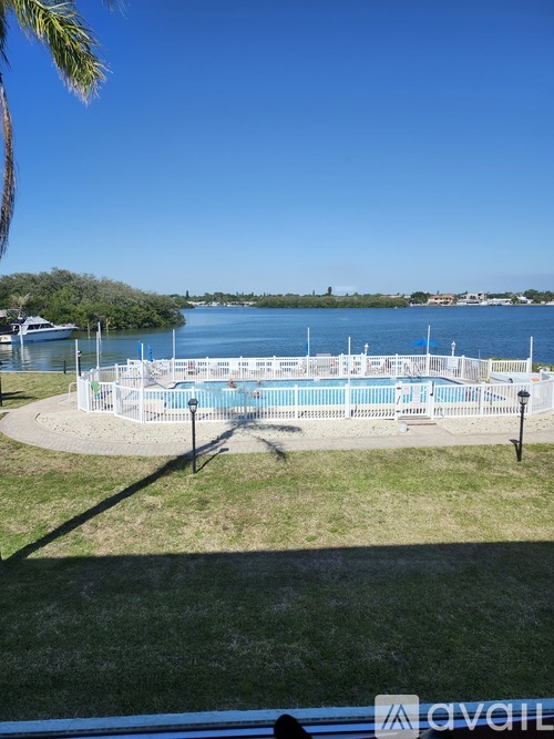 A pool surrounded by a white fence with a view of the water and trees in the background.