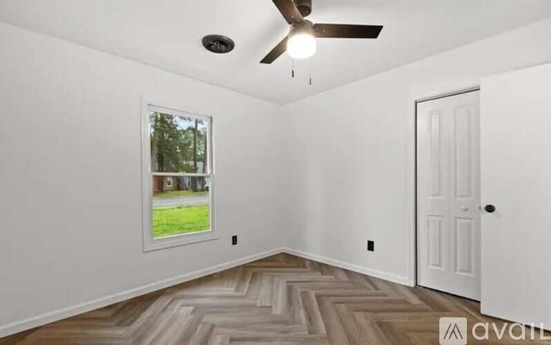 A room with a ceiling fan and a window showing a view of a house and trees.