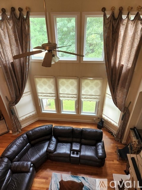A living room with a black leather couch and a fan.