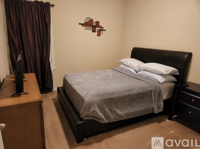 A bedroom with a large bed, a wooden cabinet, and a wall art of a birdhouse.