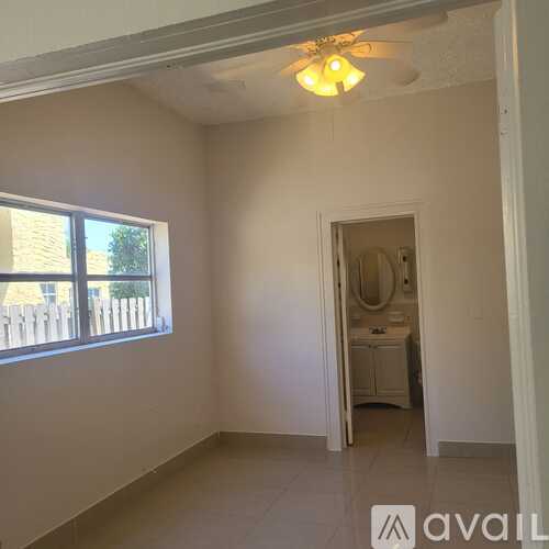 A room with a window and a bathroom visible through the door.