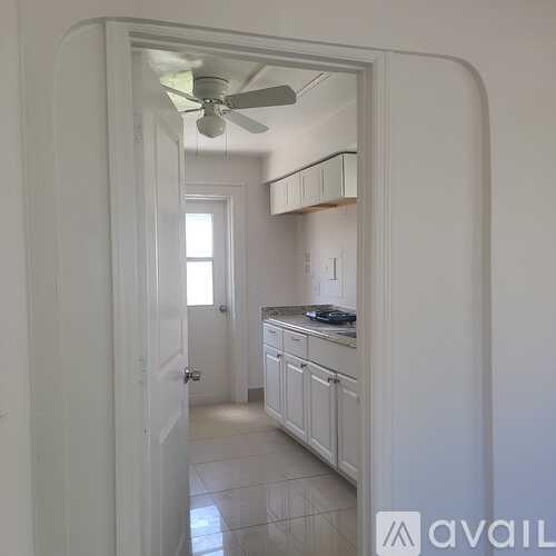 A white doorway opens to a kitchen with a fan on the ceiling.