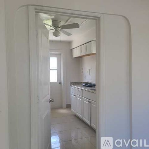A white doorway opens to a kitchen with a fan on the ceiling.
