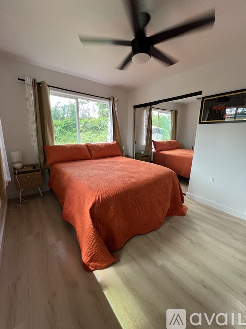 A bedroom with a bed covered in an orange sheet and a ceiling fan.