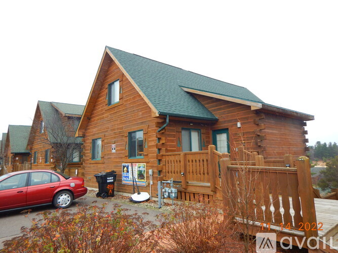 A red car is parked in front of a wooden house.