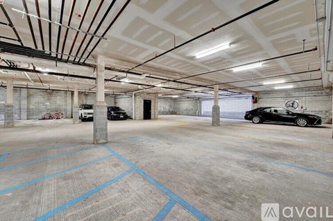 A spacious garage with a concrete floor and a high ceiling, equipped with a car lift and a parked black car.