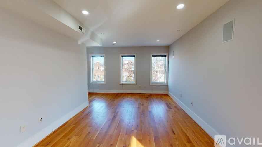 A spacious room with wooden floors and three windows.