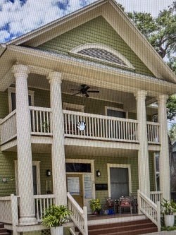 A green house with a white porch and a ceiling fan.