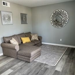 A grey couch with a yellow pillow is in the middle of a room with a grey floor and a grey wall.