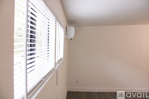 A room with a window covered by white blinds and a smoke detector on the wall.