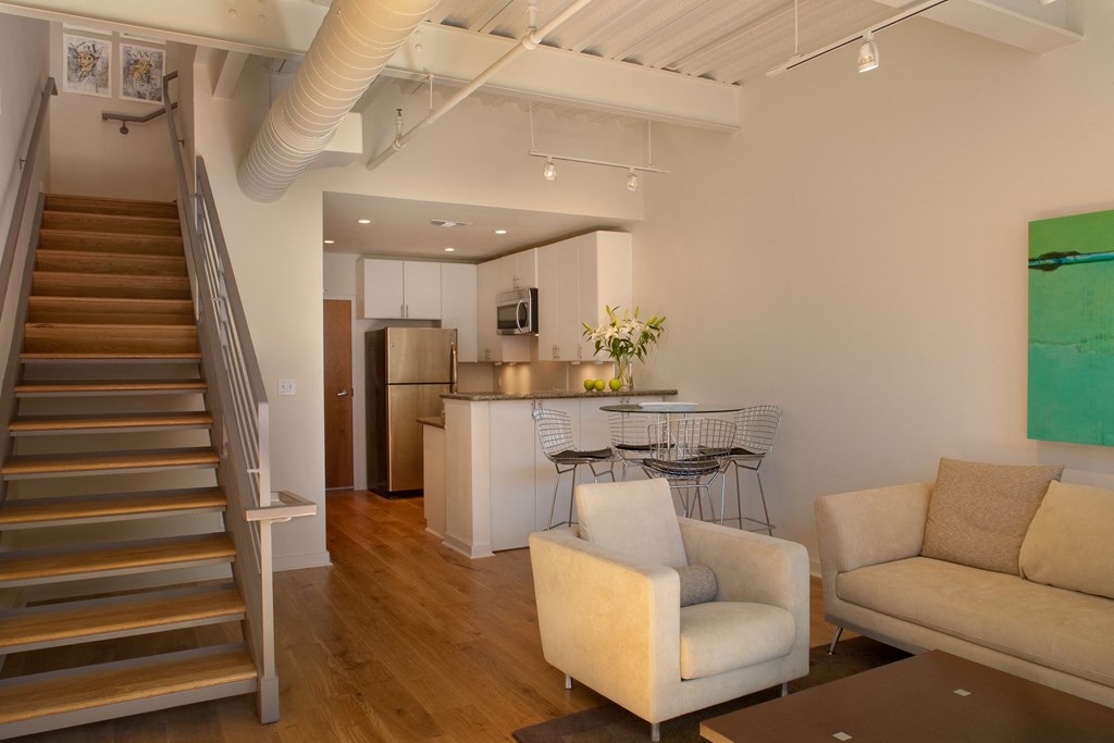 a living room with a staircase and a kitchen with a table and chairs
