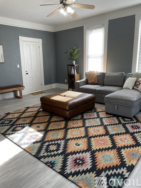 A living room with a grey couch, a brown ottoman, and a rug with a geometric pattern.