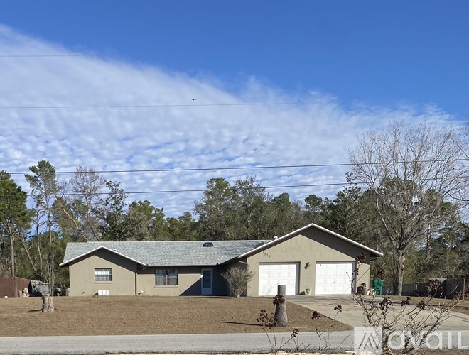 A house with a brown roof and a white garage door is in front of a green trash can.